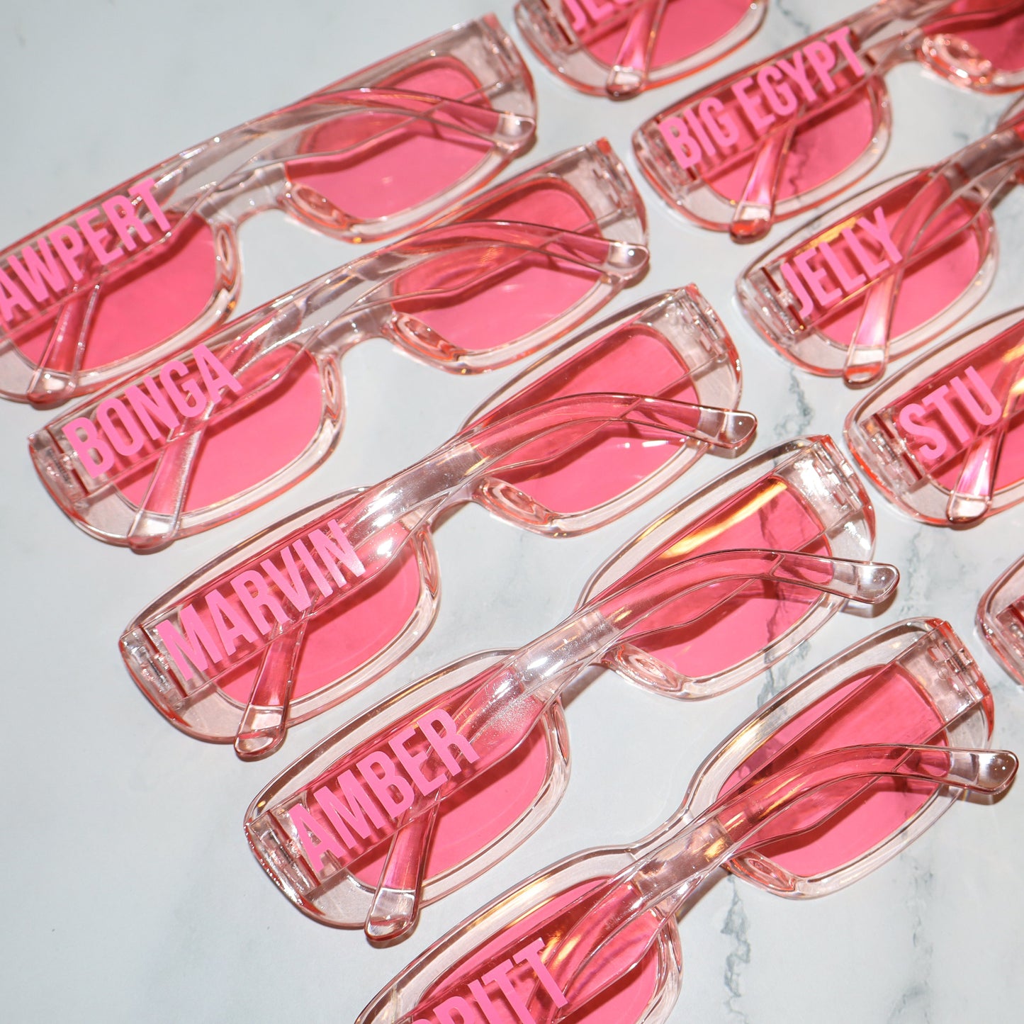 Pink sunglasses with names on a marble surface