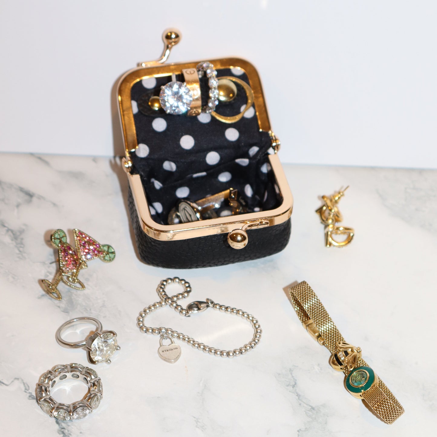 Jewelry set including a black polka dot case, bracelets, and rings on a marble surface