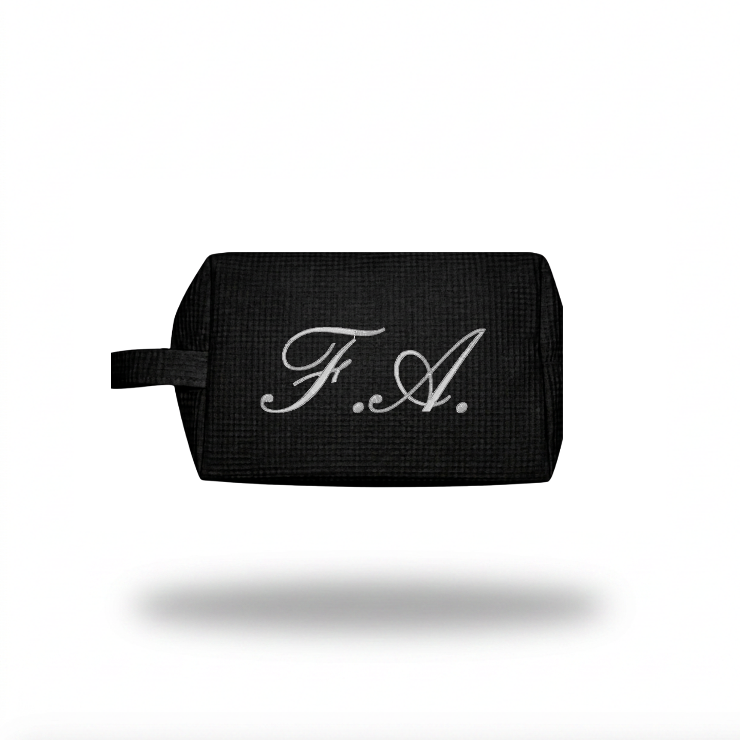 A black textured rectangular pouch with a small loop handle and a white embroidered script monogram reading 'F.A.