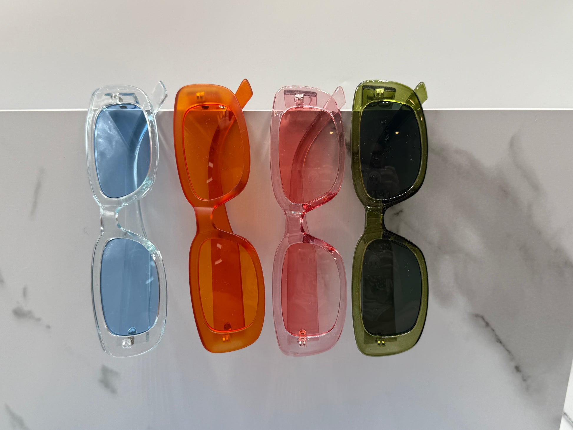 Four pairs of sunglasses in different colors on a marble surface