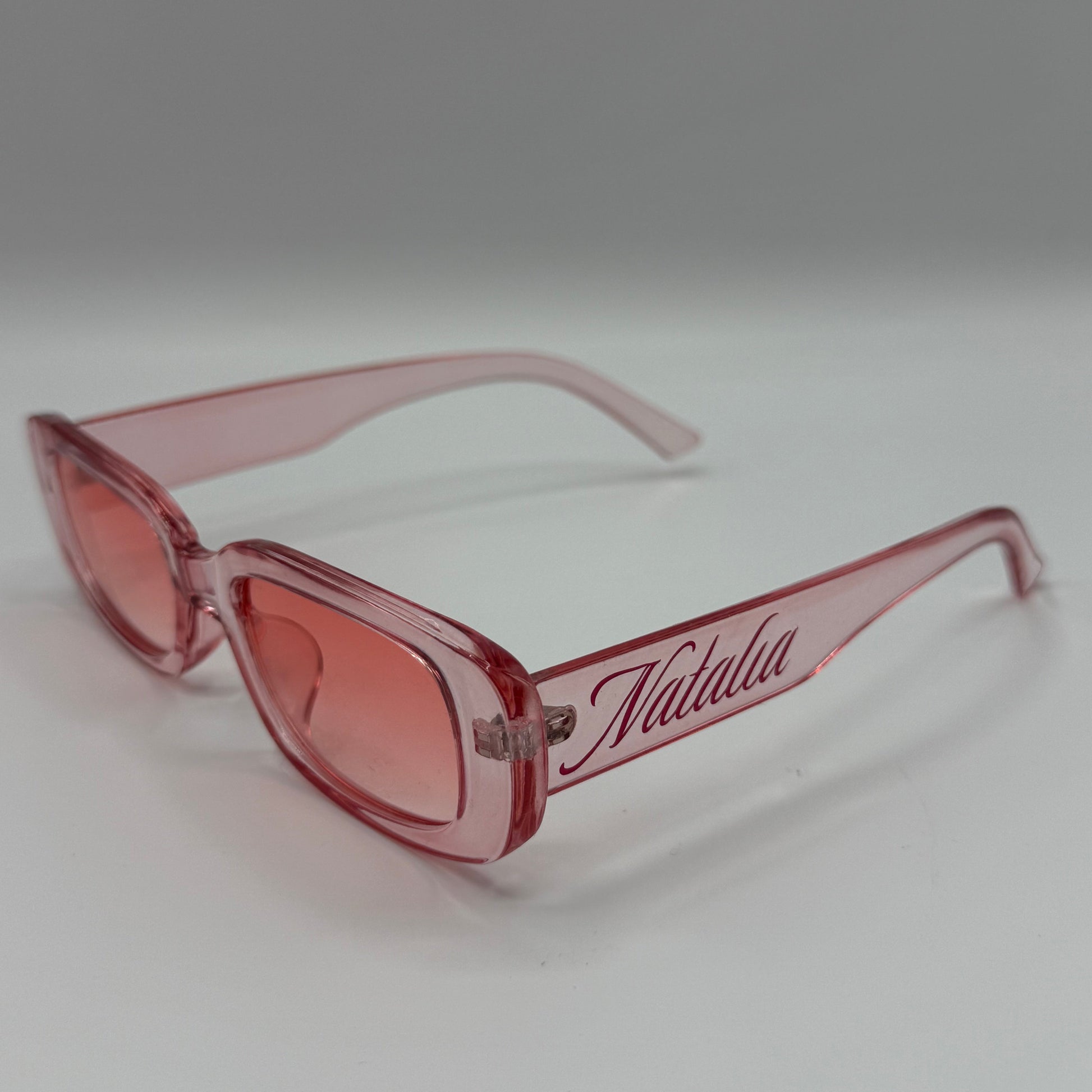 Pink sunglasses with 'Frida' branding on a white background