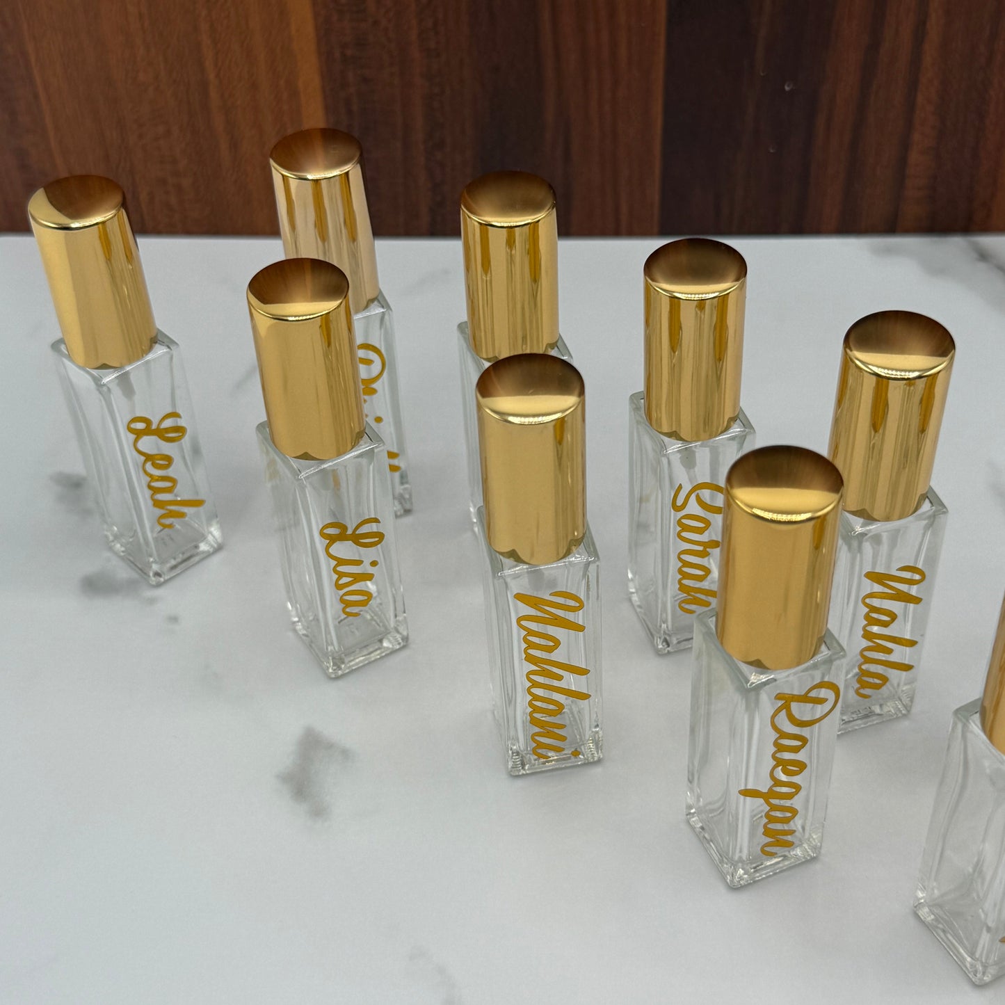 Small clear bottles with gold caps labeled with names on a marble surface.