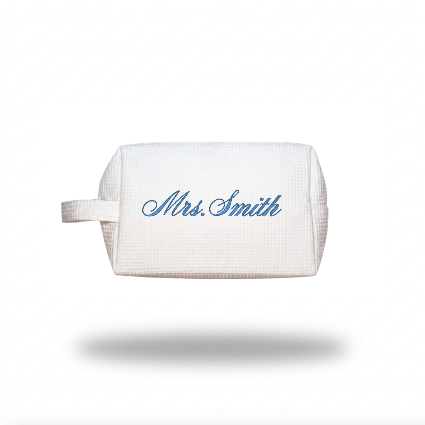 A white waffle-weave cosmetic pouch with a handle, featuring the name 'Mrs. Smith' embroidered in blue cursive script on the front, shown against a plain white background with a soft drop shadow.