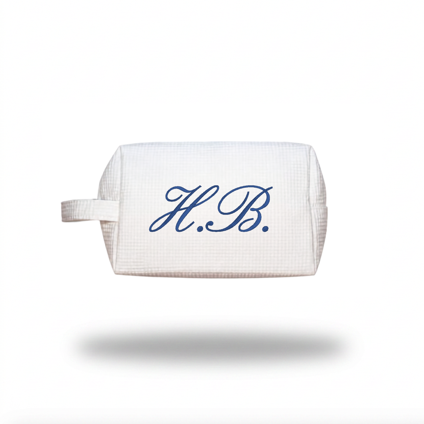 A white waffle-weave cosmetic pouch with a blue embroidered monogram 'H.B.