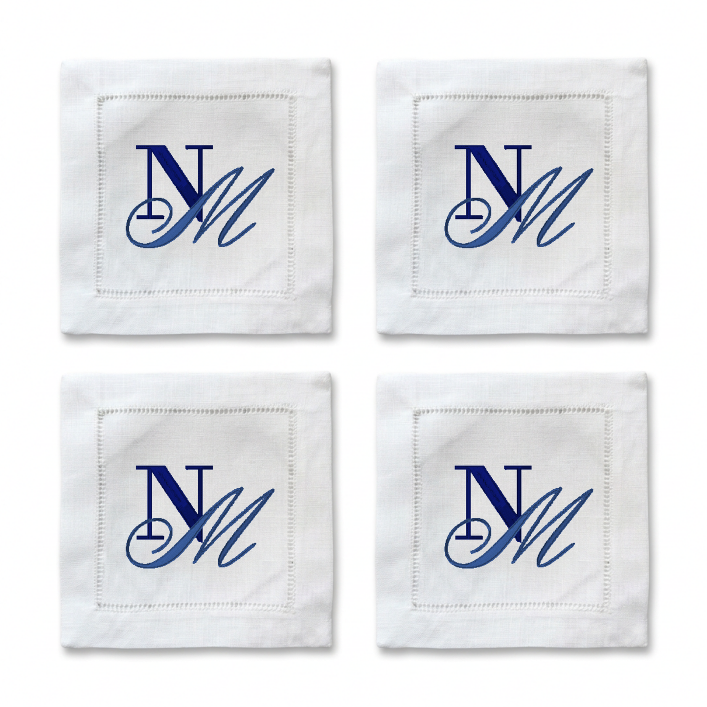 Four white square napkins arranged in a 2x2 grid, each with a stitched border and a blue embroidered monogram reading 'NM'.