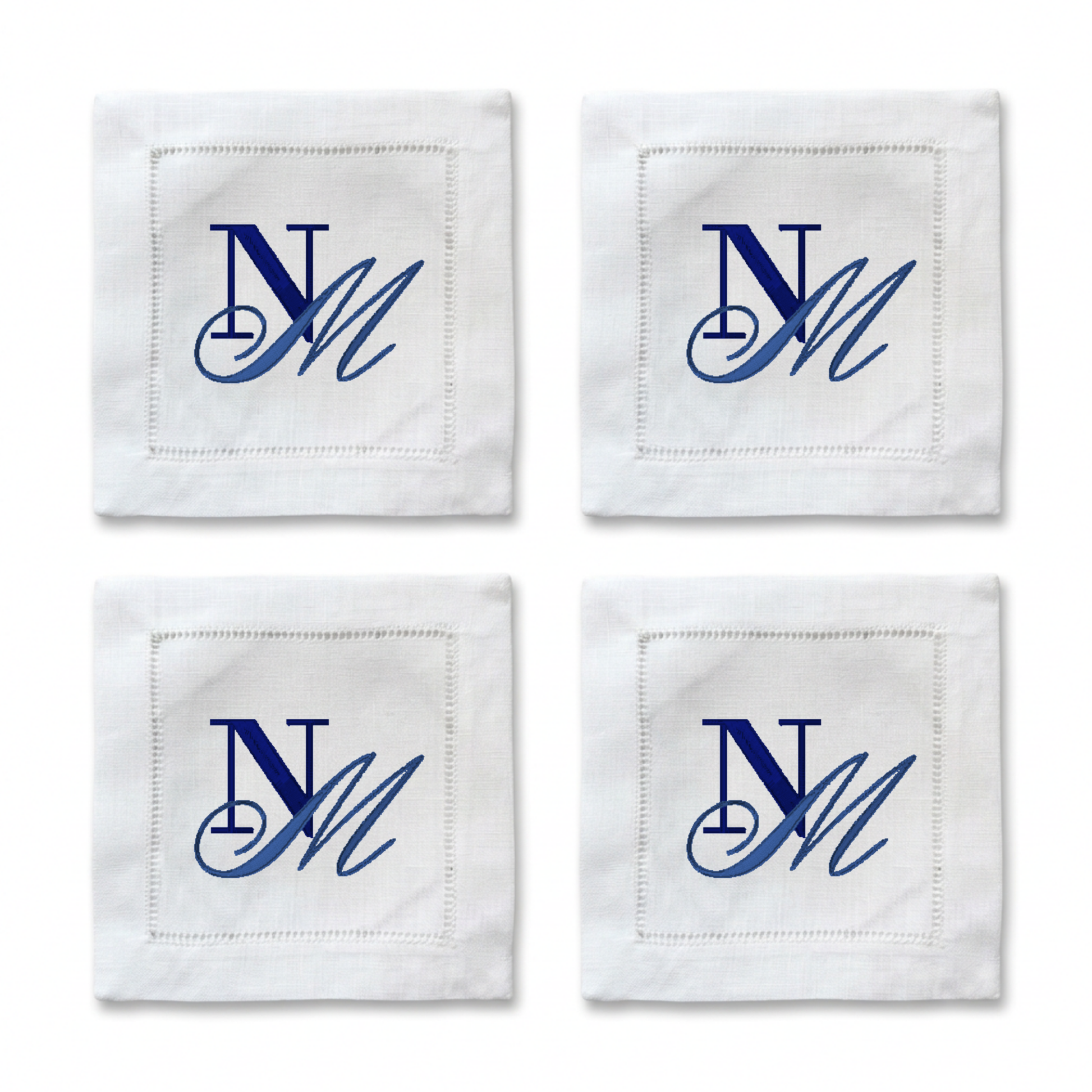 Four white square napkins arranged in a 2x2 grid, each with a stitched border and a blue embroidered monogram reading 'NM'.