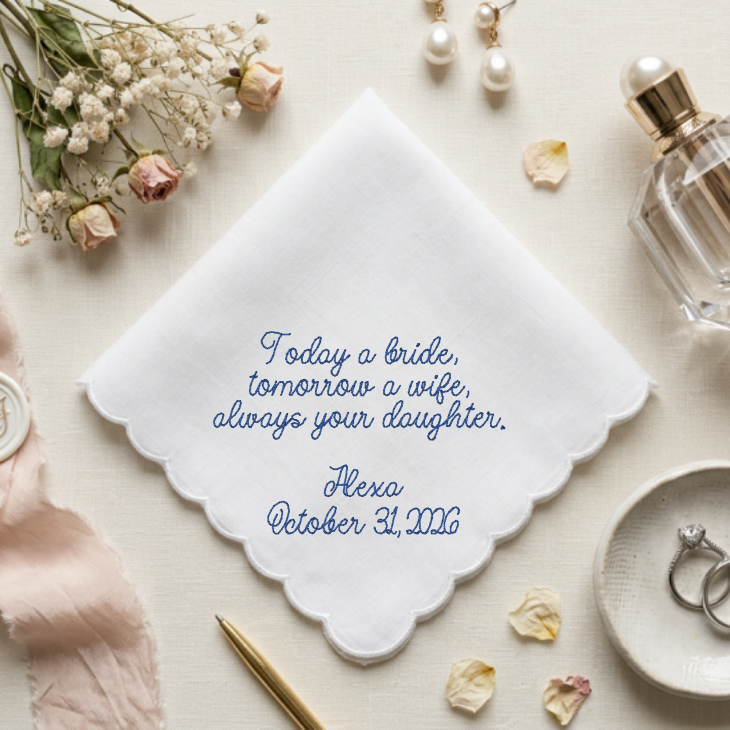A white embroidered bridal napkin with scalloped edges and blue script text reading, 'Today a bride, tomorrow a wife, always your daughter. Hexa October 31, 2026.