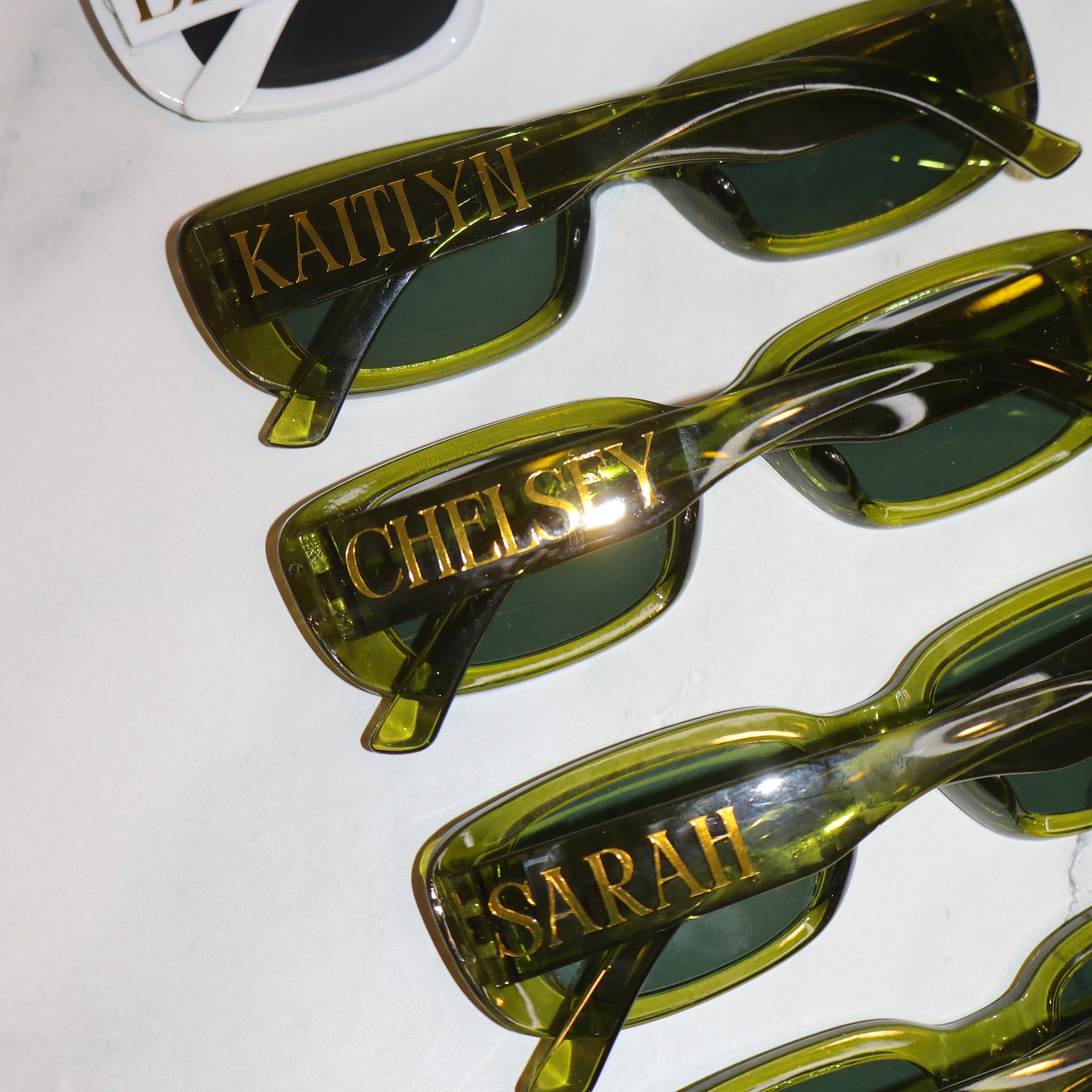 Set of green sunglasses with gold accents and brand names on a white background