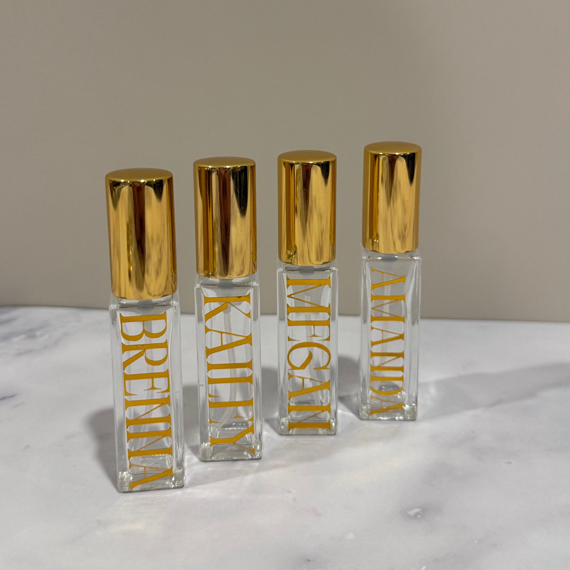 Set of clear lip gloss tubes with gold caps on a marble surface