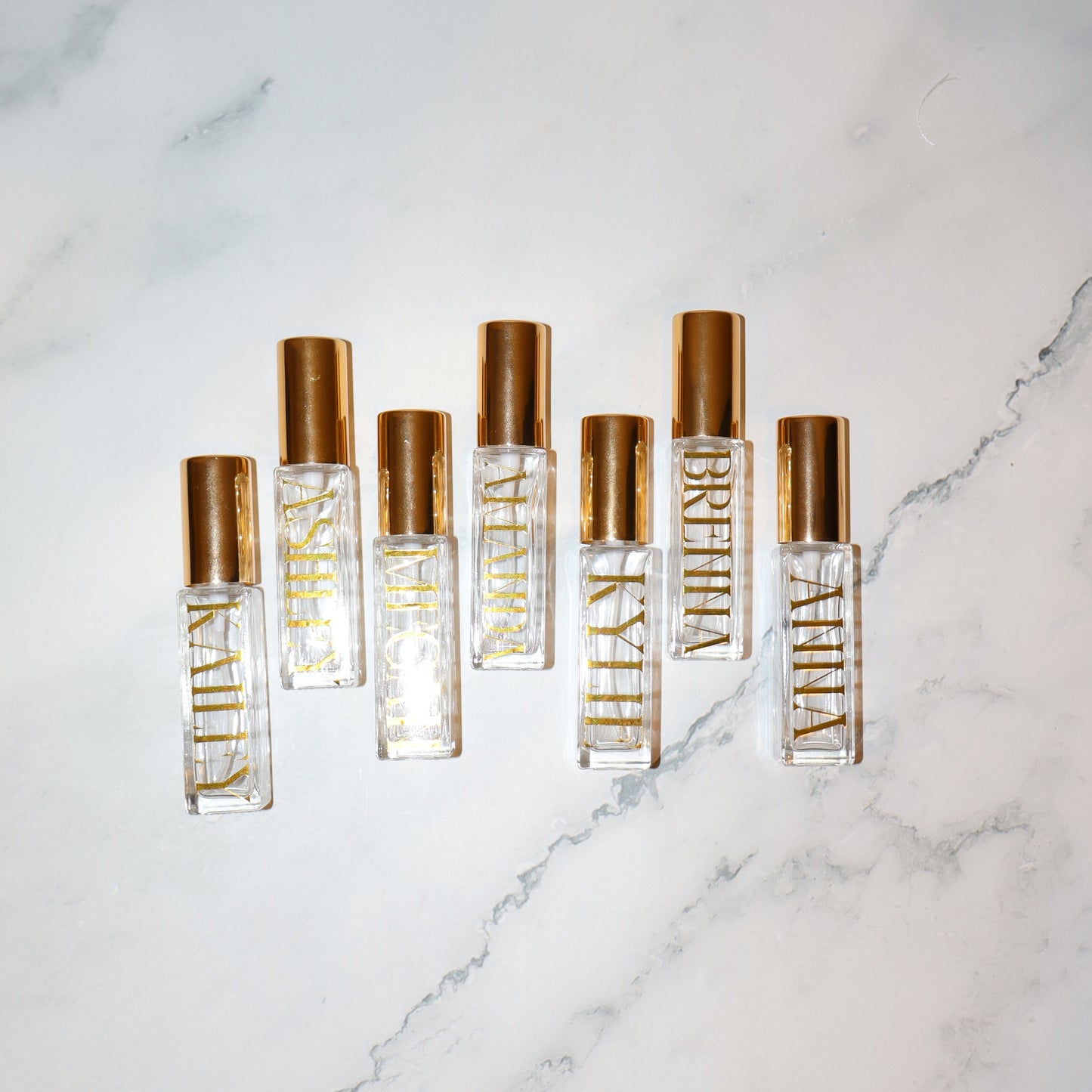 Five gold and clear perfume bottles on a marble surface
