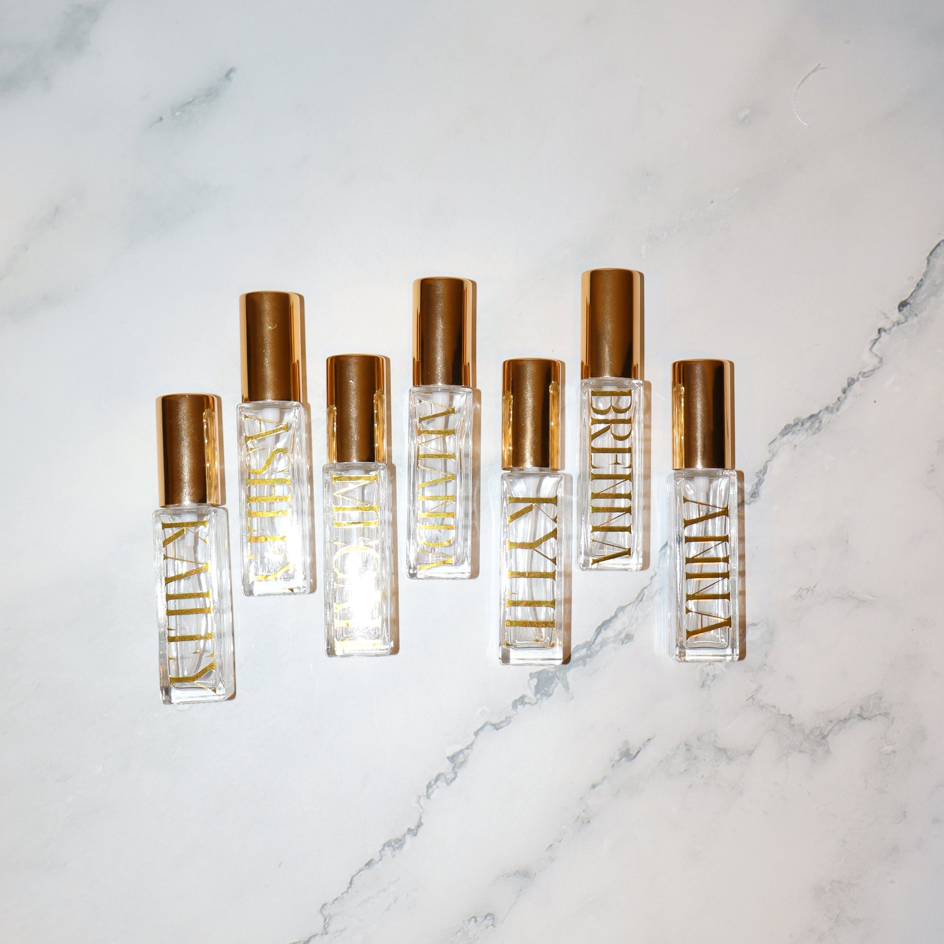 Five gold and clear perfume bottles on a marble surface