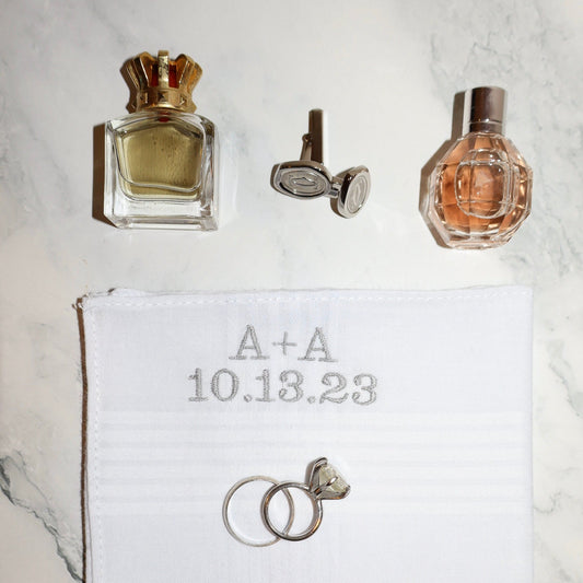 Two perfume bottles, a couple of rings, and a piece of paper with 'A+A 10.13.23' on a marble surface.
