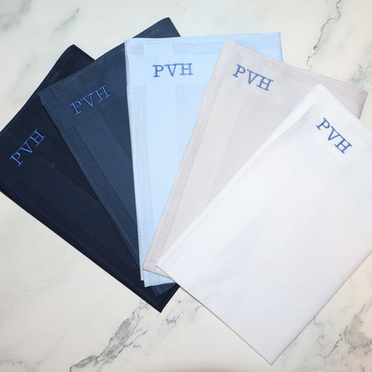 Set of folded handkerchiefs with initials branding on a marble surface