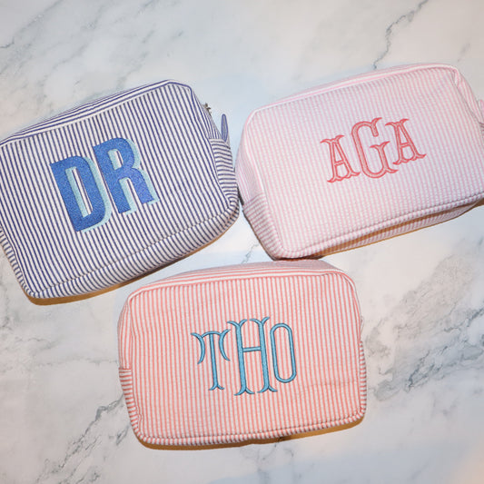 Three striped pouches with monogrammed initials on a marble surface