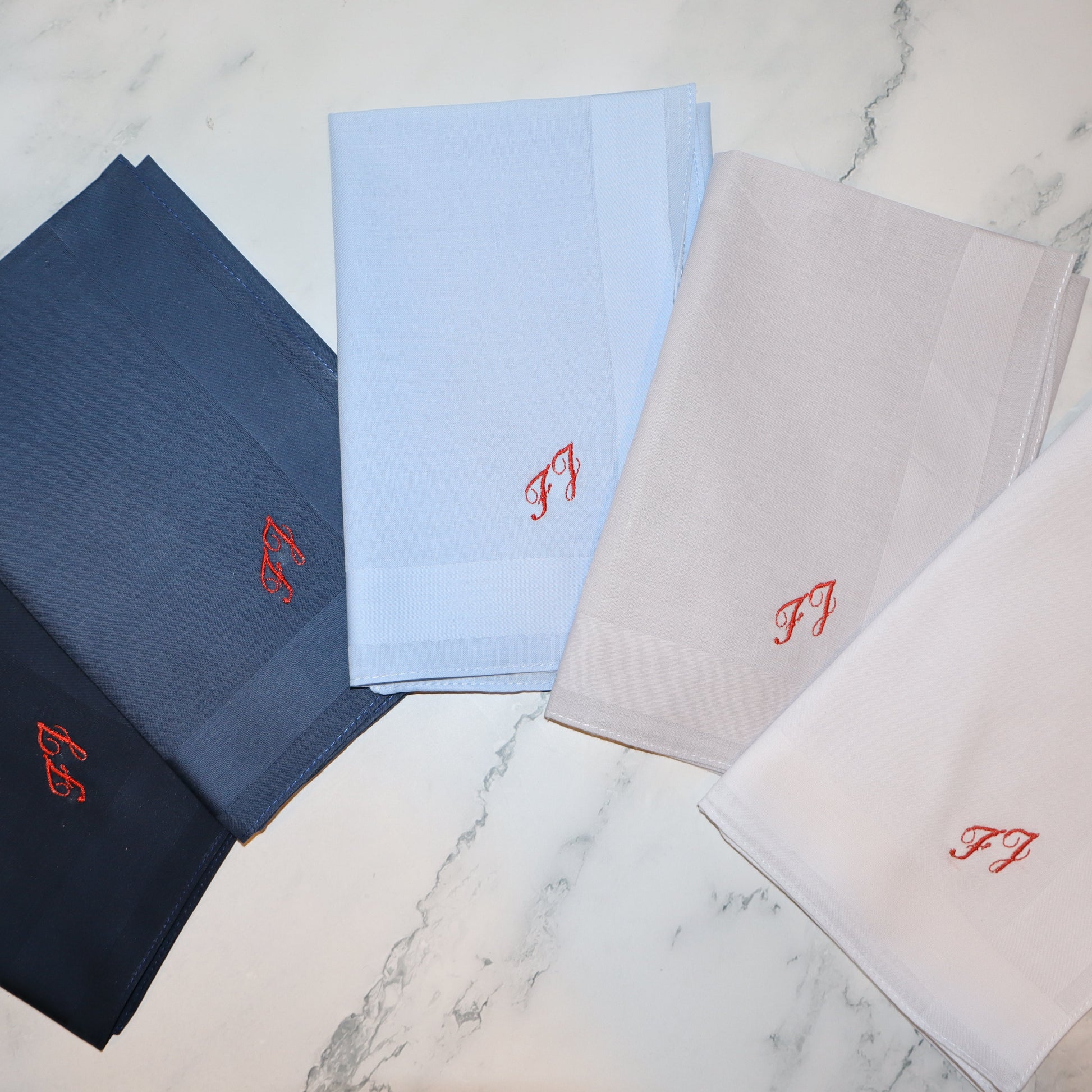 Set of folded handkerchiefs in black, blue, and gray with red logos on a marble surface.