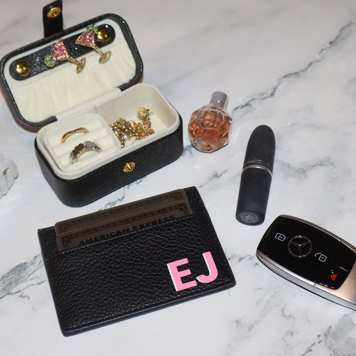 Jewelry box with jewelry, lipstick, perfume bottle, and car key fob on a marble surface.