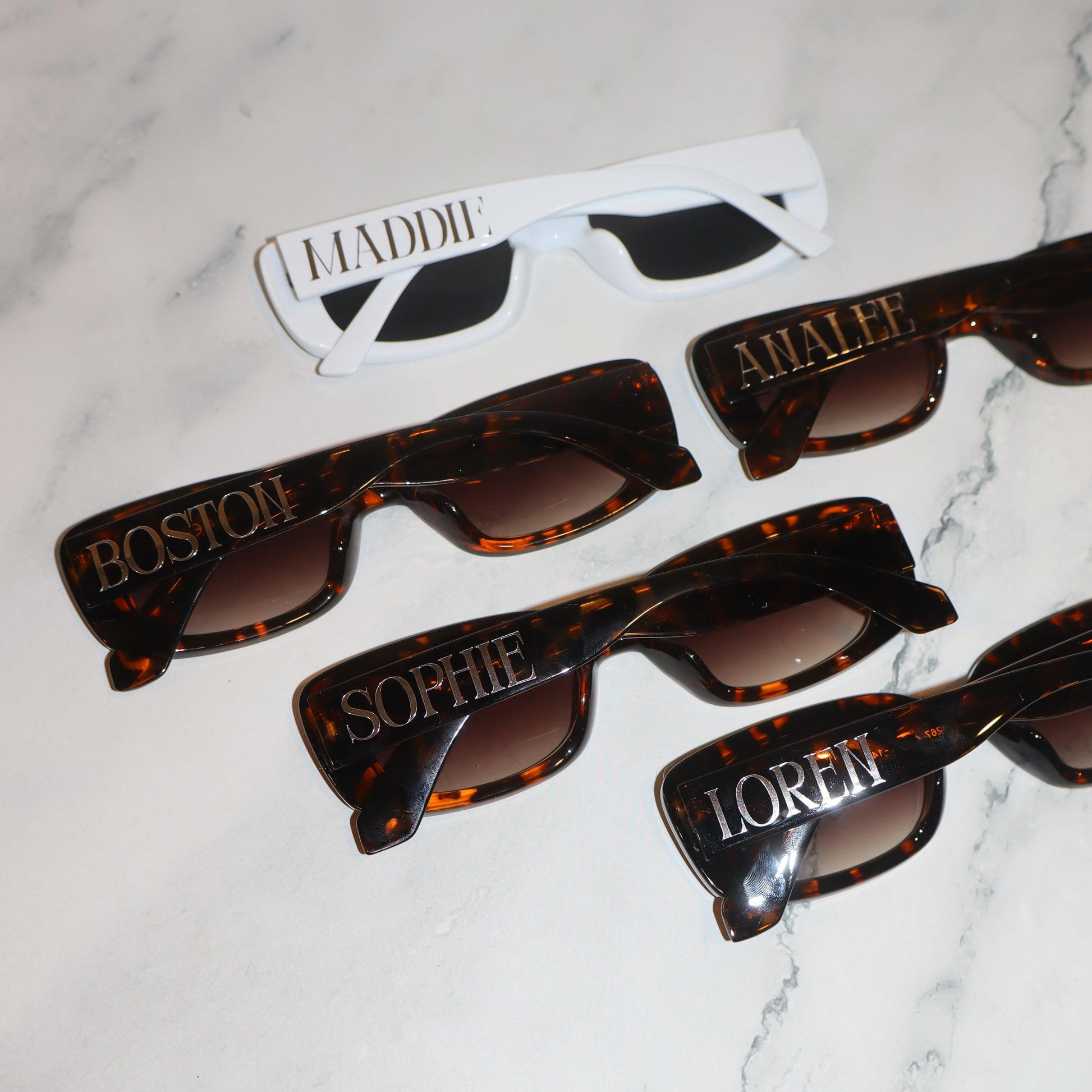 Tortoiseshell sunglasses with personalized names on a marble surface