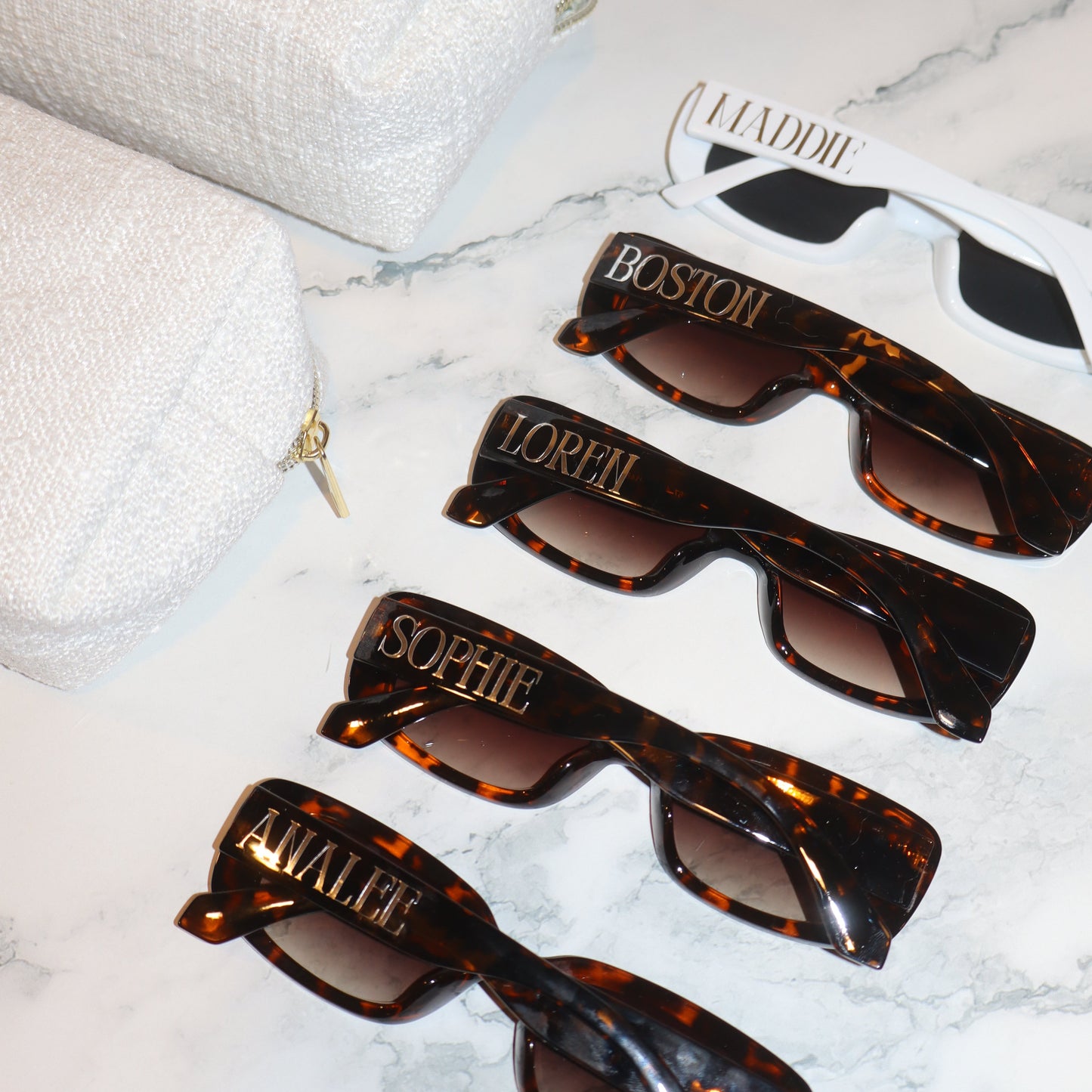 Set of tortoiseshell sunglasses with personalized names on a white marble surface