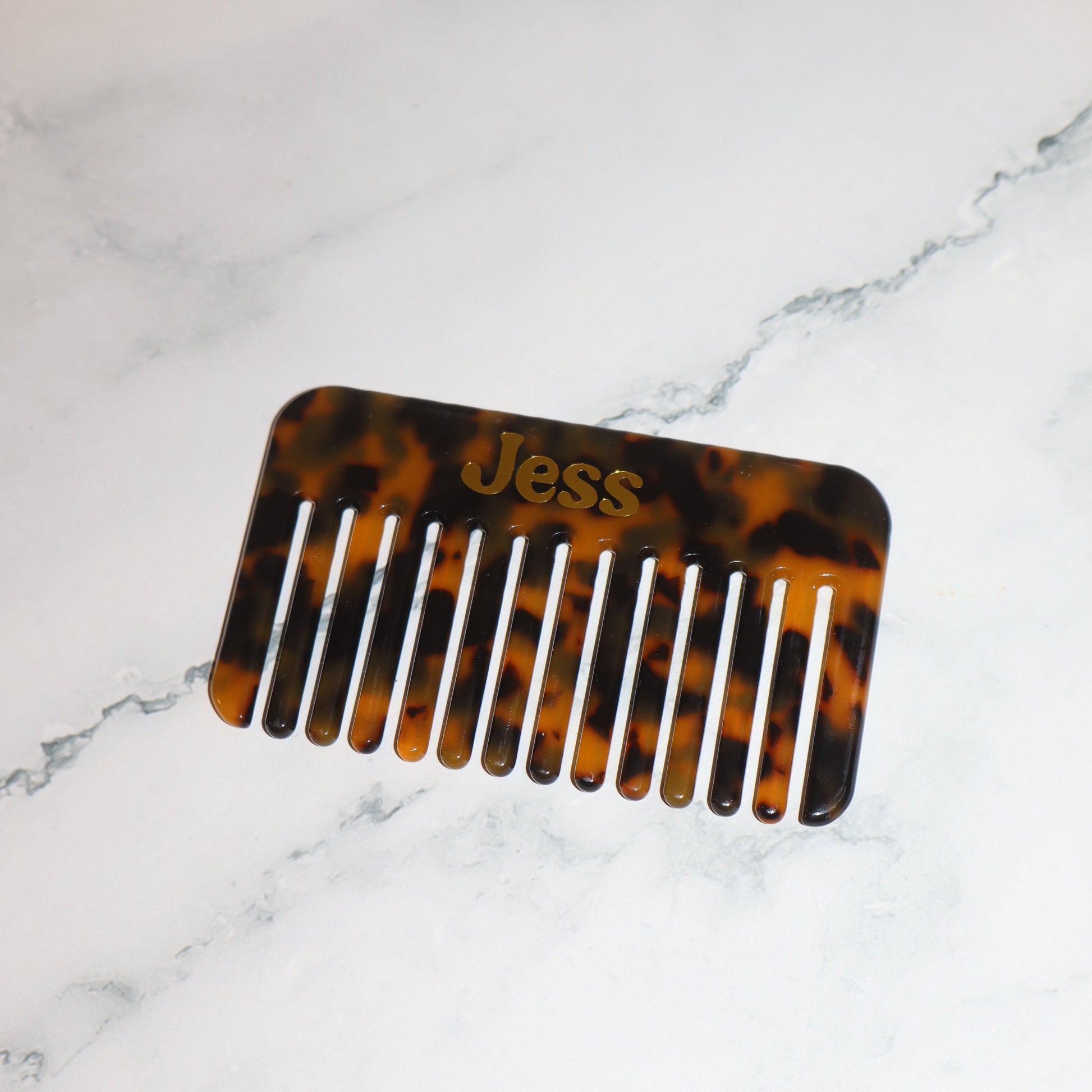 Tortoiseshell comb with 'Jess' engraved on a marble surface
