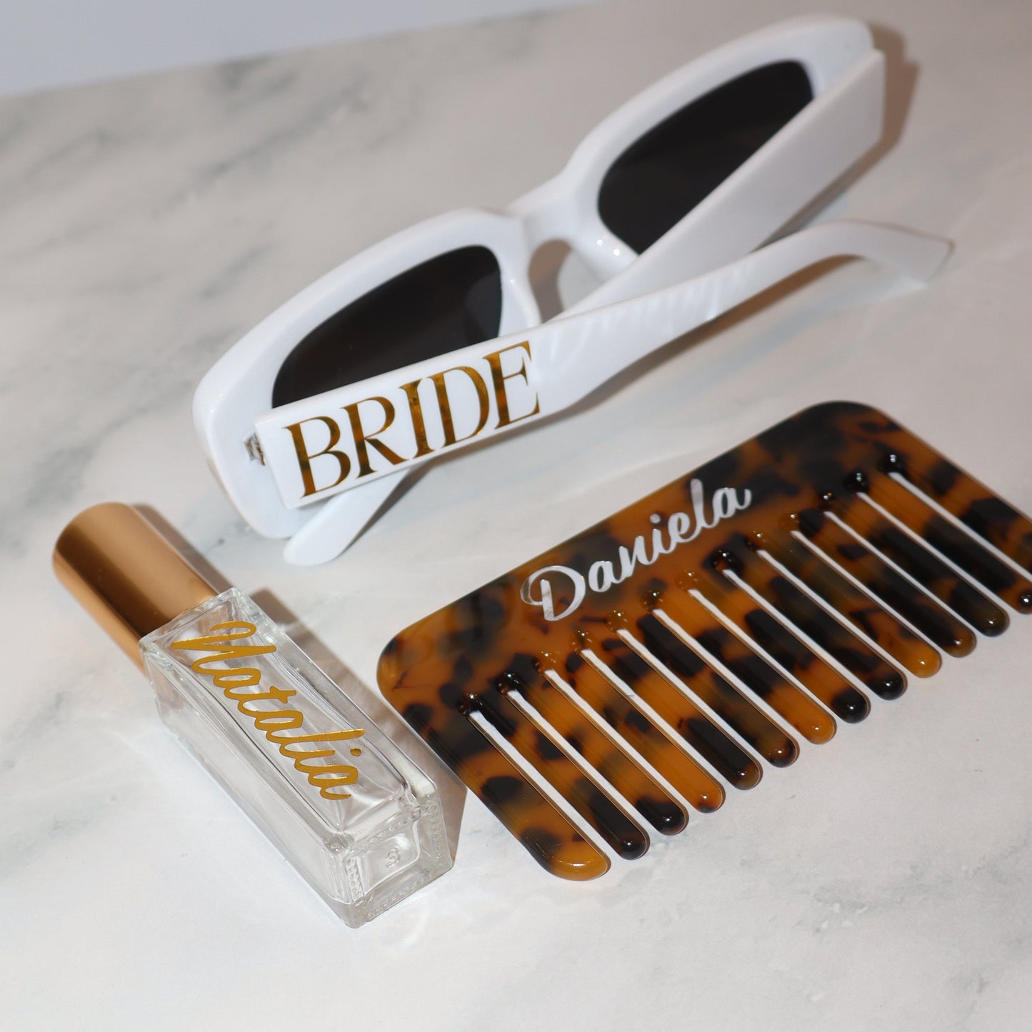 Personalized comb, sunglasses, and bottle cap on a marble surface